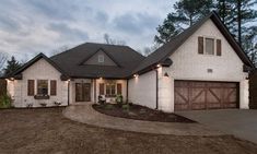 a white brick house with brown shutters on the front and garage doors open to let in light