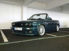 a blue bmw convertible parked in a parking lot next to a white wall and black floor