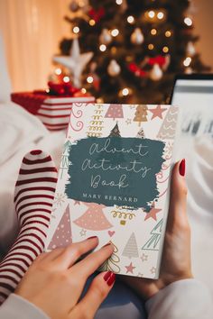 a woman is holding a book in front of a christmas tree with presents on it