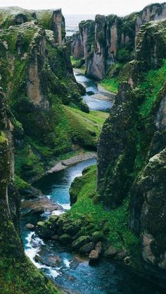 a river flowing through a lush green valley next to tall rock formations in the distance