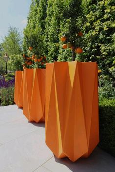 three large orange vases sitting on top of a cement ground next to bushes and trees