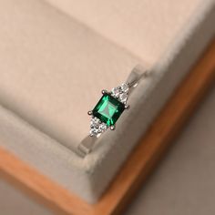 an emerald colored ring with three diamonds on the side in a white gift box that is open