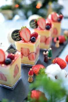 small desserts with strawberries and blueberries are on a tray next to christmas trees