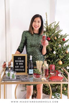 a woman standing in front of a christmas tree holding up a wine glass and bottle