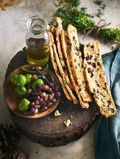 olives and bread are on a wooden plate next to a bottle of olive oil