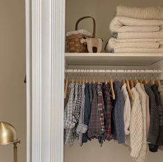 an open closet with folded clothes hanging on the rack and a basket next to it