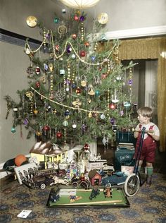 a young boy standing in front of a christmas tree with toys and ornaments on it