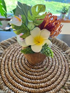 an arrangement of flowers is sitting on a wicker place mat in front of a window