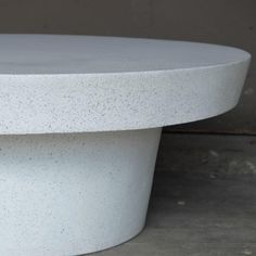 a white round table sitting on top of a cement floor next to a wall or window