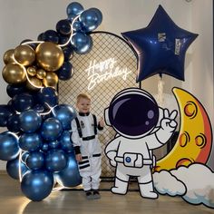 a young boy in an astronaut suit standing next to balloons