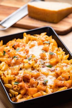 a casserole dish filled with pasta and cheese on a cutting board next to bread