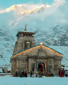 a group of people standing in front of a building with snow on the mountains behind it