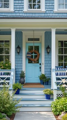 a blue house with white trim and front porch, potted plants on the steps