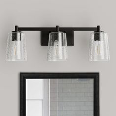 three light bathroom fixture with clear glass shades and black metal frame, on a gray wall