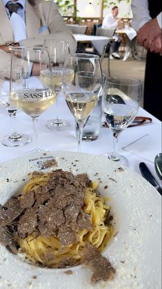 a white plate topped with pasta and meat next to wine glasses