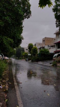 an empty street with cars parked on the side and trees lining the road in the background