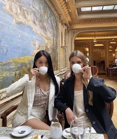 two women sitting at a table drinking from cups