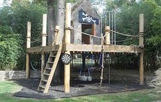 a wooden play structure with pirate flags on the roof and ladders to climb up