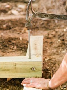 a person using a hammer to build a wooden structure in the ground with dirt and grass