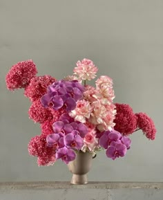 a vase filled with pink and purple flowers on top of a wooden table next to a wall