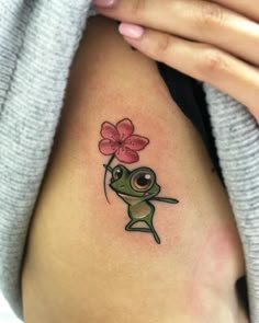 a woman with a tattoo on her arm holding a flower in the shape of a frog