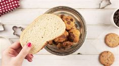 a person holding a piece of bread in front of some cookies and other food items