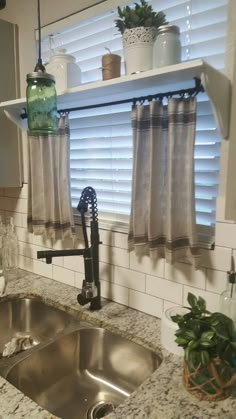 a kitchen sink with a faucet next to a window covered in curtains and potted plants