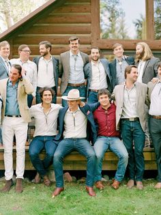 a group of men posing for a photo in front of a log cabin with their arms around each other