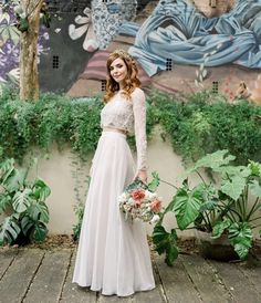 a woman standing in front of a mural wearing a white dress and holding a bouquet