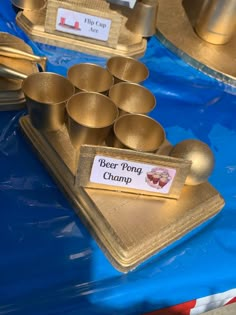 there are many gold cups and trays on the blue table cloth that is covered with plastic