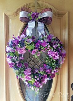 a wreath with purple flowers hanging on the front door to give it a festive feel