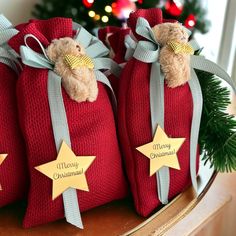 three red christmas bags with teddy bears in them on a table next to a christmas tree