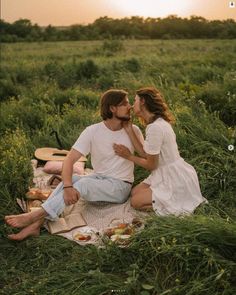 a man and woman are sitting on a blanket in the middle of a grassy field