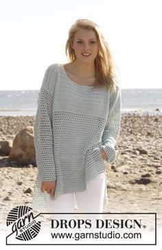 a woman standing on top of a sandy beach next to the ocean wearing a green sweater