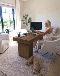 a woman sitting at a desk with her dog on the rug in front of her