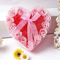 a heart shaped box filled with pink roses next to a small white flower and a gold frame