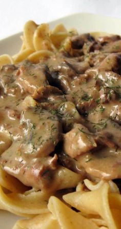 a white plate topped with pasta covered in gravy and mushrooms on top of it