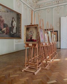 there are many paintings on easels in the middle of a room with wood flooring