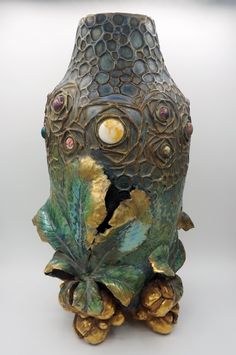 a vase with gold and green decorations on it's sides, sitting on a white surface