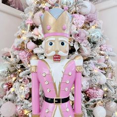 a pink and gold nutcracker statue in front of a christmas tree with ornaments