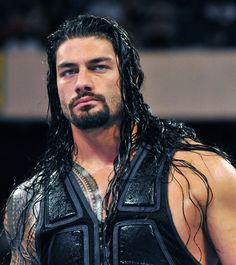 a man with long hair and no shirt on standing in front of a crowd wearing a leather vest