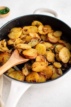 a pan filled with cooked potatoes on top of a white counter next to a wooden spoon