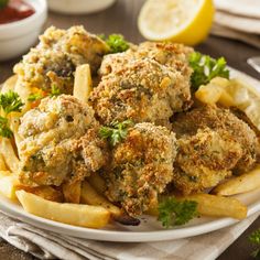 a white plate topped with fried chicken and french fries next to lemon wedges on a table