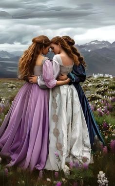 two women in long dresses hugging each other on a field with mountains in the background