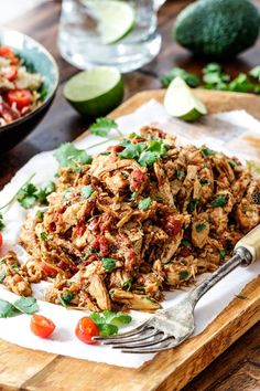 shredded meat with tomatoes and cilantro on a cutting board