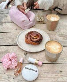 there is a cinnamon roll on the table next to two cups of coffee and other items