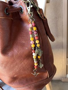 a brown leather purse with colorful beads and charms hanging from it's side pocket