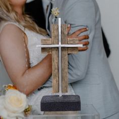 a newly married couple hugging each other in front of a wooden cross on a table