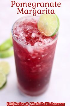 a close up of a drink in a glass with limes on the side and text that reads pomegranate margarita