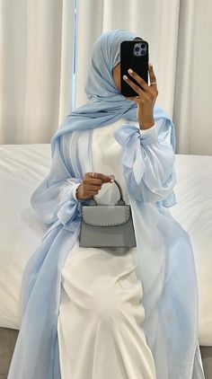 a woman wearing a blue hijab and holding a cell phone in her hand